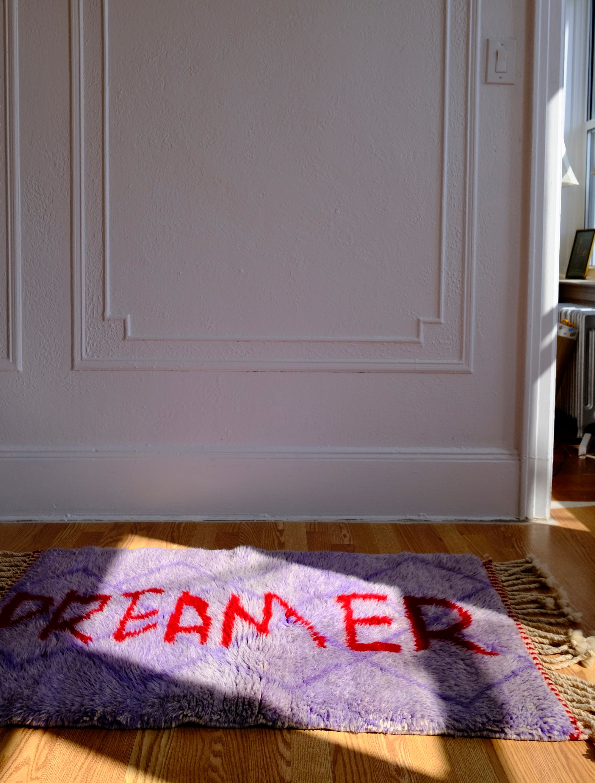 Experience the elegance of our 'Royal Dreamscape Rug,' featuring a handwritten 'Dreamer' in red yarn. The light purple base is intricately woven with a subtle Berber pattern, creating a truly unique and enchanting addition to your space. Elevate your decor with this regal blend of design and craftsmanship, where classic beauty meets artistic flair.