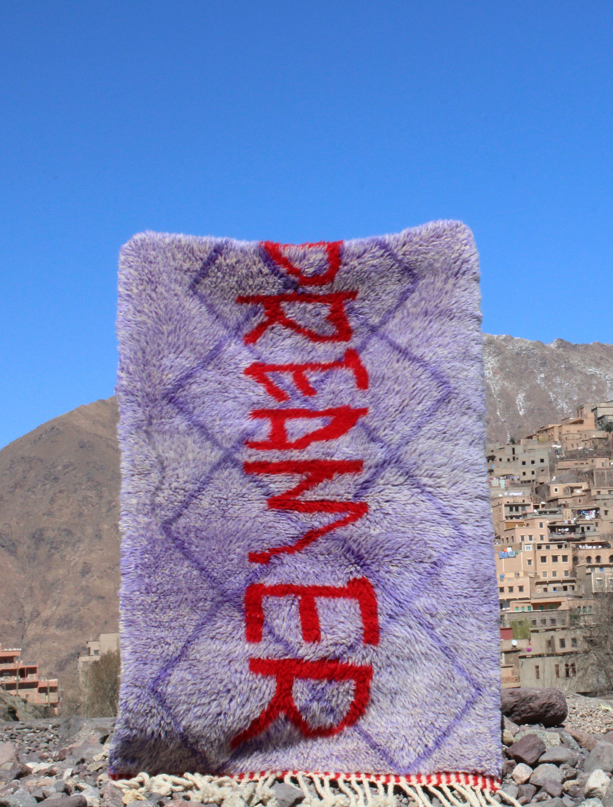 Experience the elegance of our 'Royal Dreamscape Rug,' featuring a handwritten 'Dreamer' in red yarn. The light purple base is intricately woven with a subtle Berber pattern, creating a truly unique and enchanting addition to your space. Elevate your decor with this regal blend of design and craftsmanship, where classic beauty meets artistic flair.