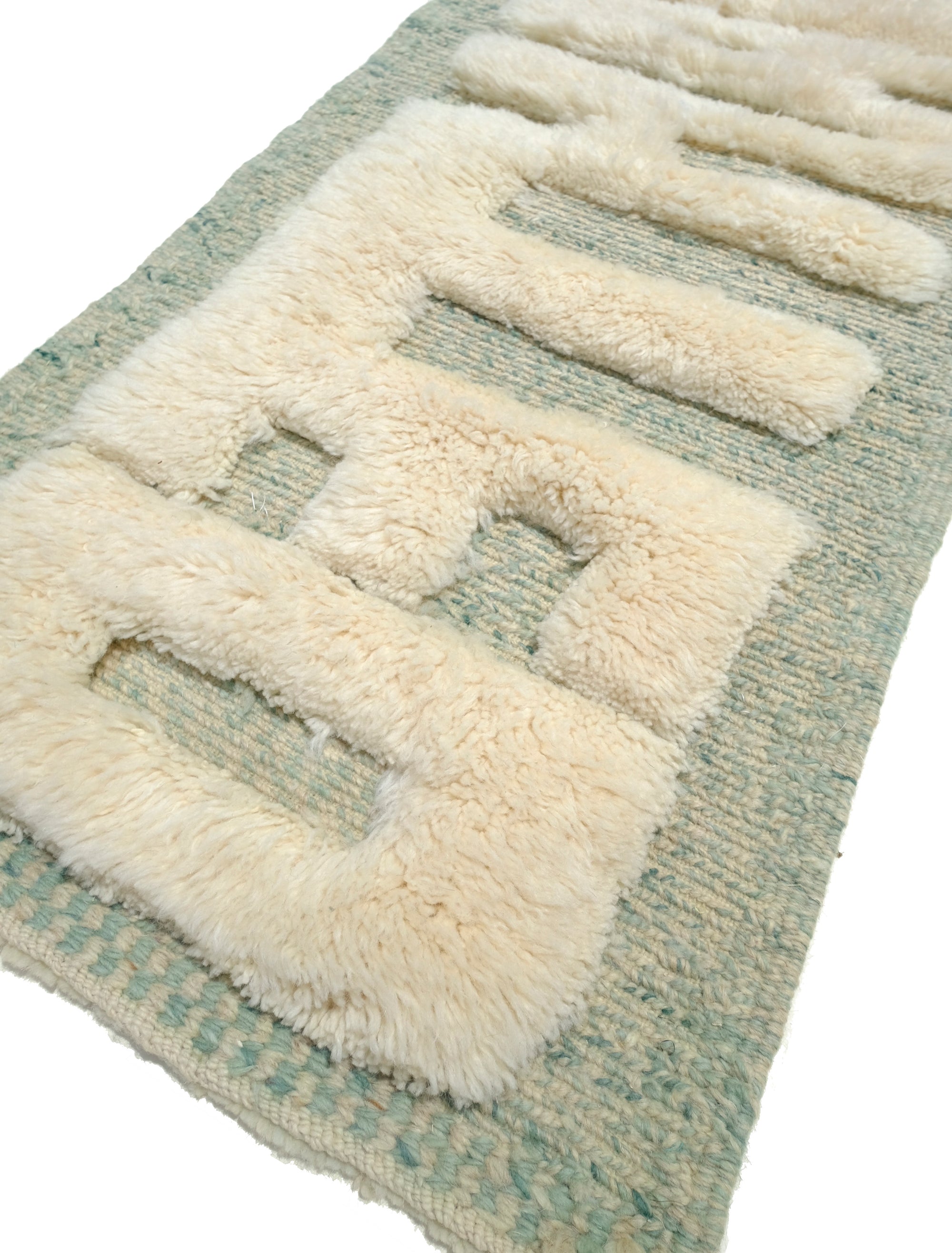 Discover the Reversible Ivory Green Whispers Rug, a truly unique and versatile piece handmade by Berber women in the Atlas Mountains. With its fuzzy 'WANTED' lettering on one side and a calming mix of pale green shades on the other, this rug adds an elegant touch to your decor while spreading a positive message. Explore the beauty of reversible design in this exceptional handmade creation.
