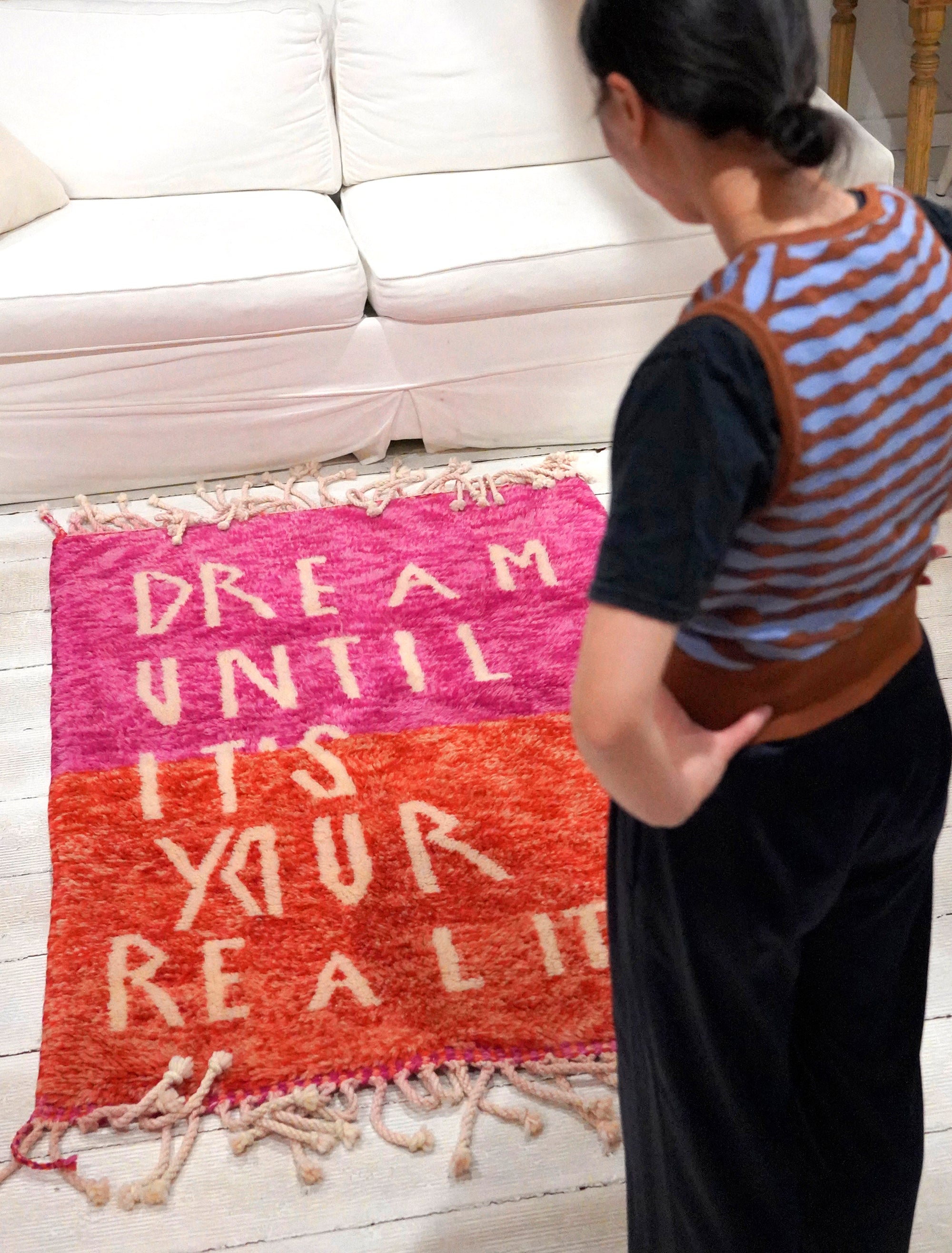 Introducing the enchanting 'Rosy Dreamscape Rug,' a delightful fusion of pink and red yarns forming a playful base, with the inspiring phrase 'Dream Until It Is Your Reality' expertly woven in white yarn. Elevate your space with this captivating blend of colors and motivational message, creating a joyful and imaginative ambiance that adds a touch of beauty and positivity to your home.