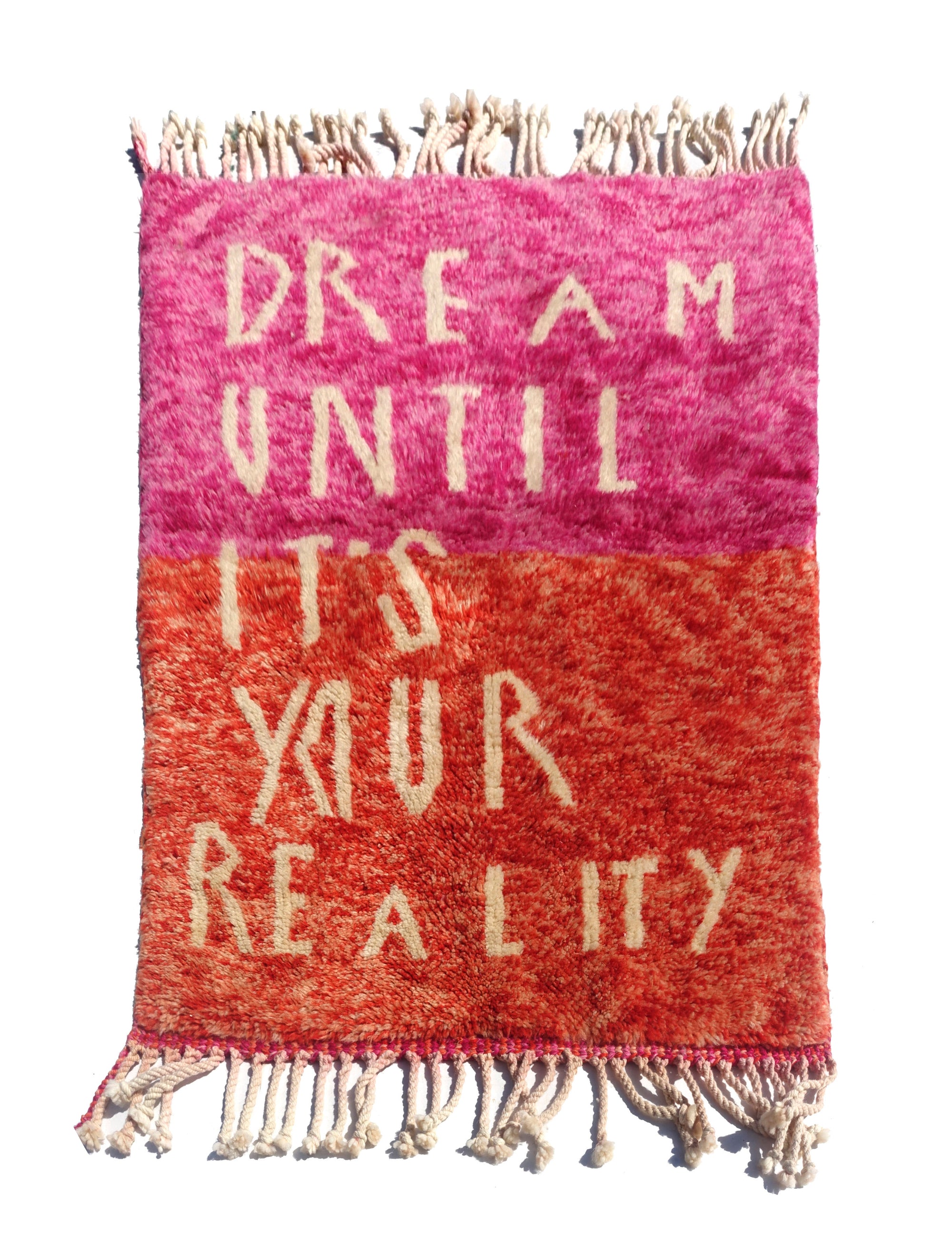 Introducing the enchanting 'Rosy Dreamscape Rug,' a delightful fusion of pink and red yarns forming a playful base, with the inspiring phrase 'Dream Until It Is Your Reality' expertly woven in white yarn. Elevate your space with this captivating blend of colors and motivational message, creating a joyful and imaginative ambiance that adds a touch of beauty and positivity to your home.